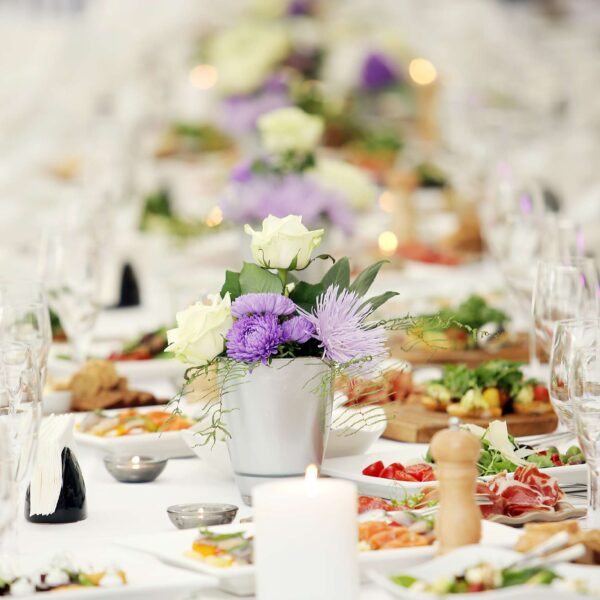 Large dining table with flowers and lots of different kinds of food at a celebration